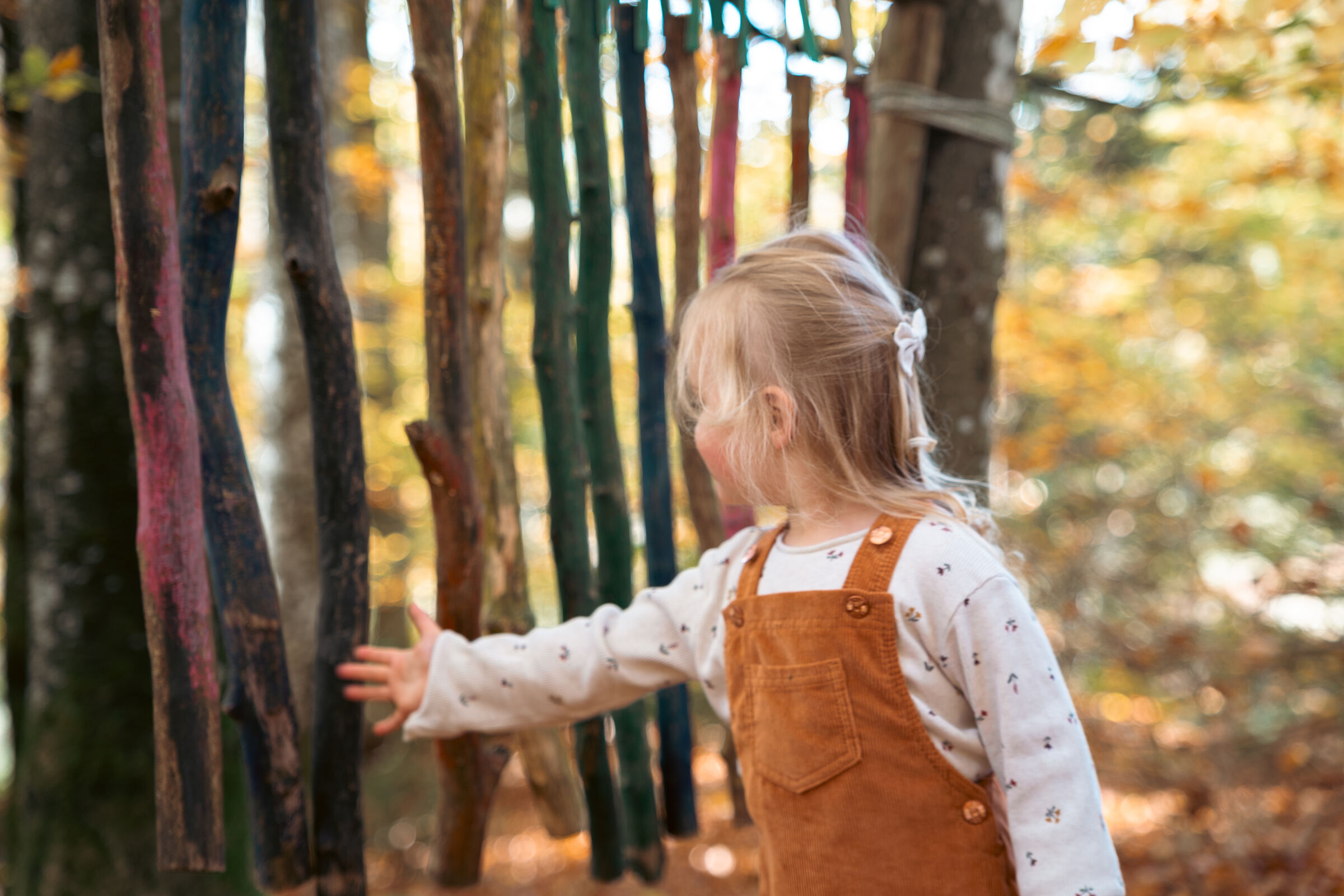 Kind spielt zwischen bunten Bändern im herbstlichen Wald